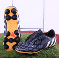 Pair of black and grey adidas Predator football boots with yellow soles displayed on artificial grass