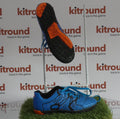 Side and sole view of kids' blue astro football boots with orange and black detailing on artificial grass