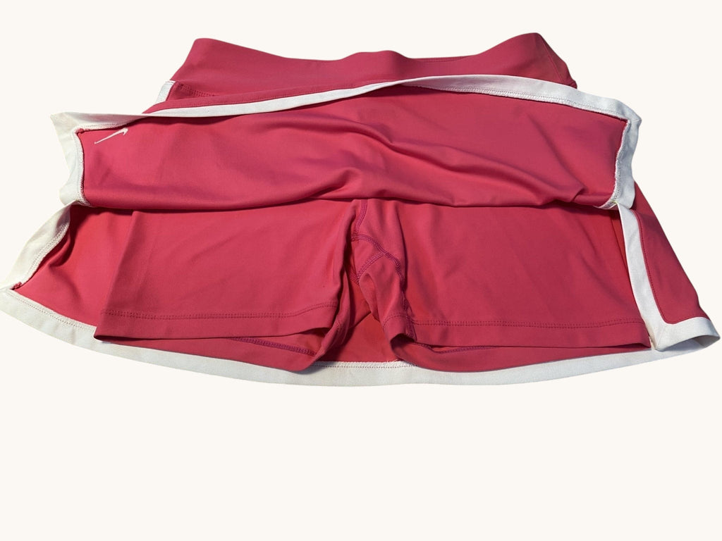 Nike pink tennis skirt with white trim and built-in shorts, featuring a small swoosh logo. Lightweight and breathable fabric.