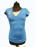 Nike women's light blue short sleeve V-neck tennis top with sponsorship logos and a cream underlayer.