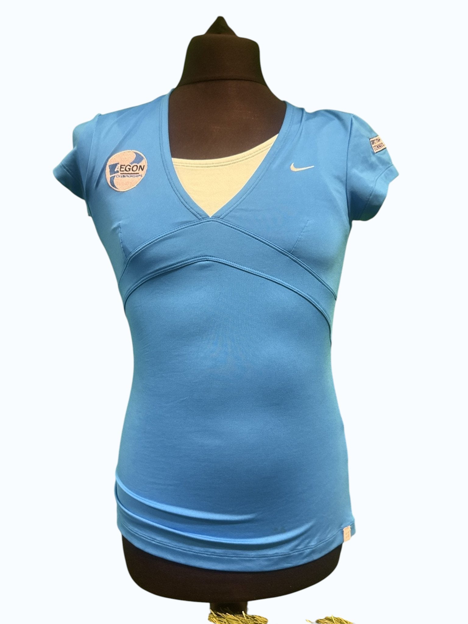 Nike women's light blue short sleeve V-neck tennis top with sponsorship logos and a cream underlayer.