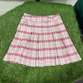Pink and white chequered pleated golf skirt laid flat on artificial grass