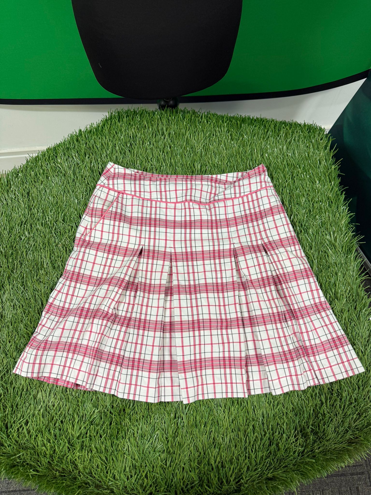 Pink and white chequered pleated golf skirt laid flat on artificial grass