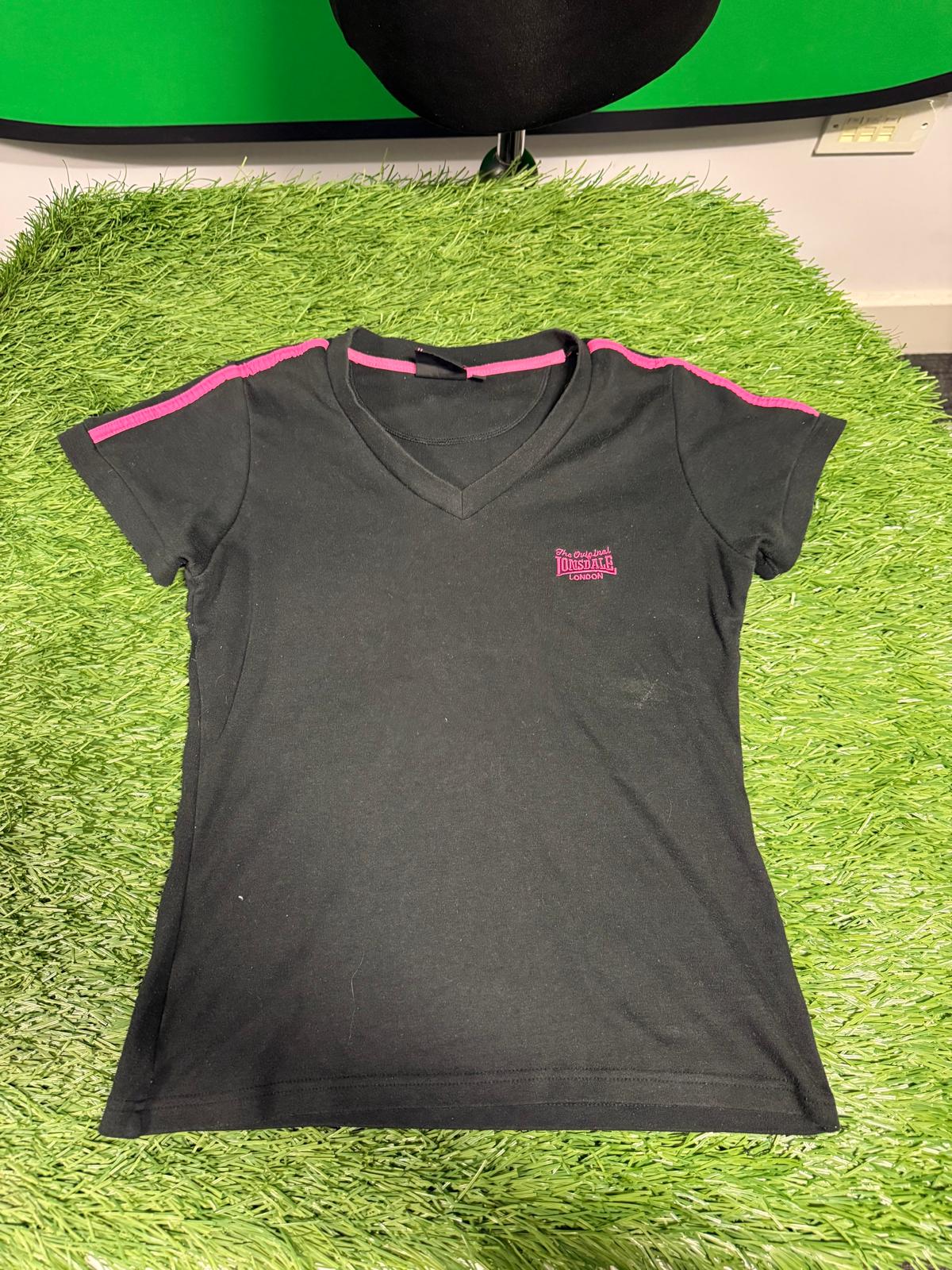 Black Lonsdale V-neck women's T-shirt with pink shoulder stripes and logo, laid flat on green artificial grass.