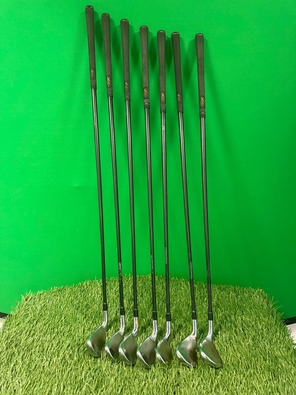 Set of seven MacGregor V Foil iron golf clubs arranged upright on artificial grass with green background
