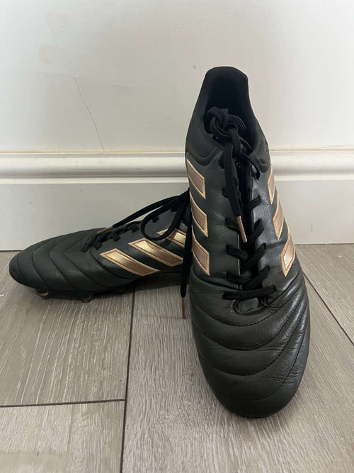 Pair of black adidas Copa football boots with gold stripes on a wooden floor