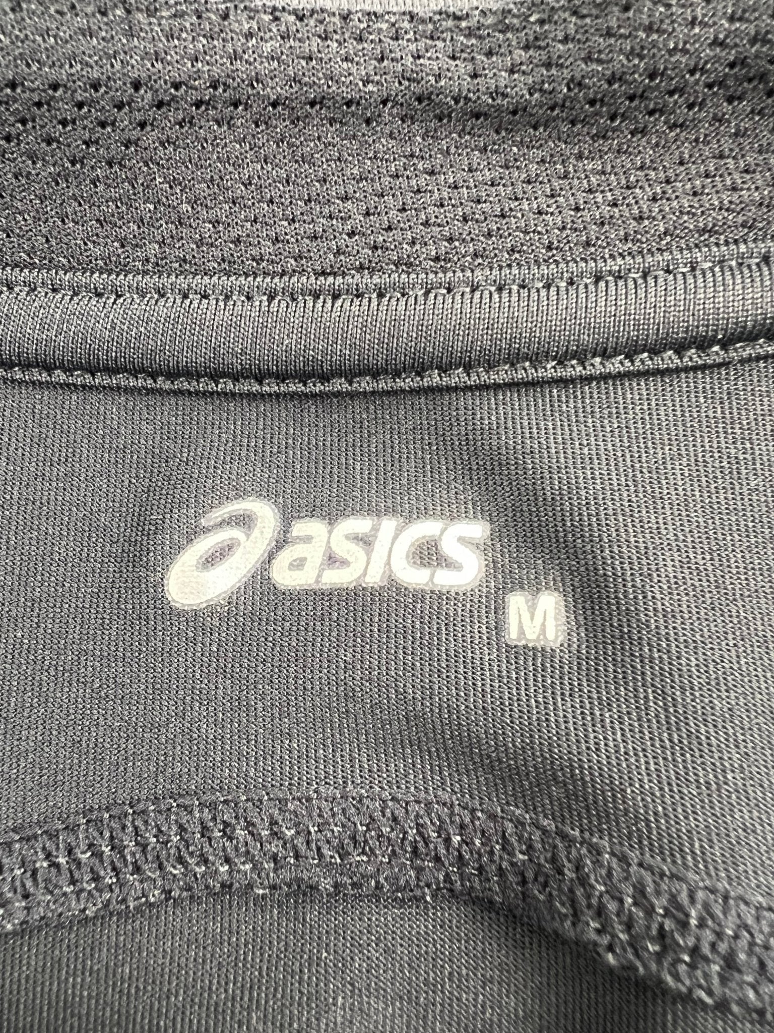 Close-up of ASICS logo and size M tag on the running top