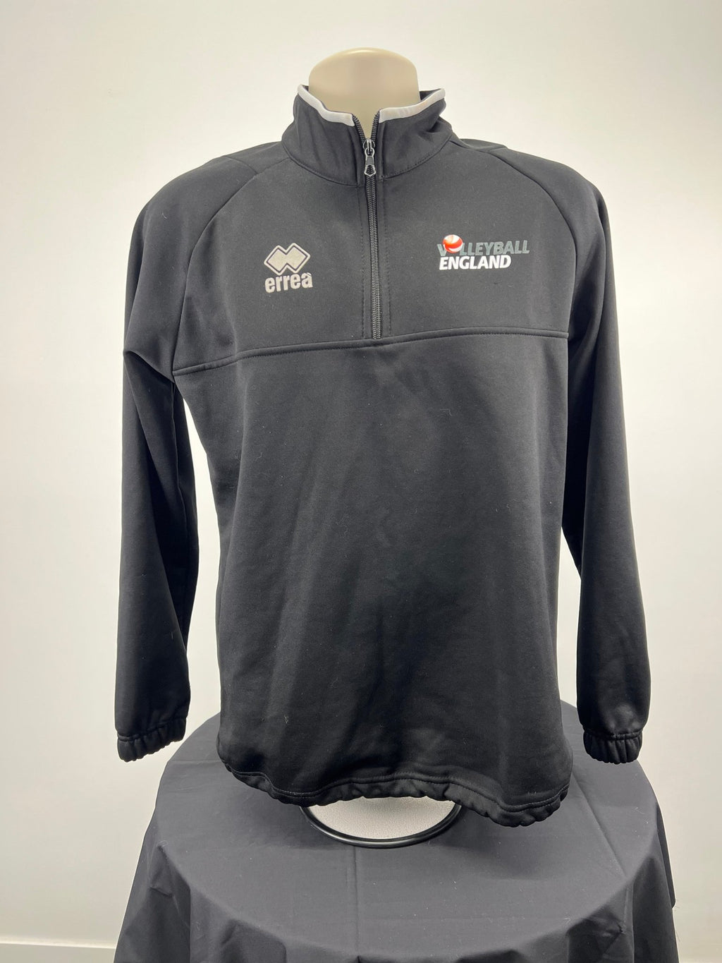 Front view of men’s black Volleyball England 1/2 zip training top with errea and Volleyball England logos