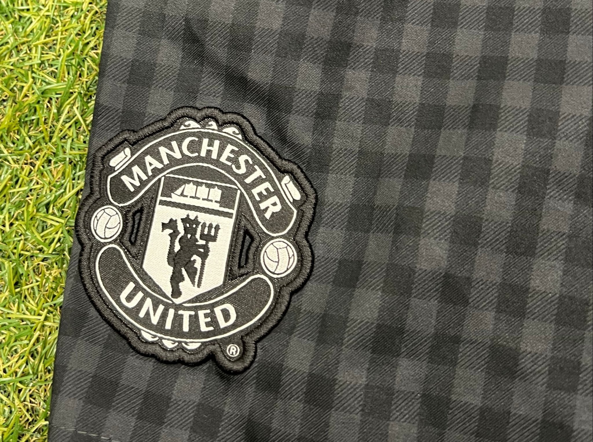 Close-up of embroidered Manchester United crest on black check Nike shorts