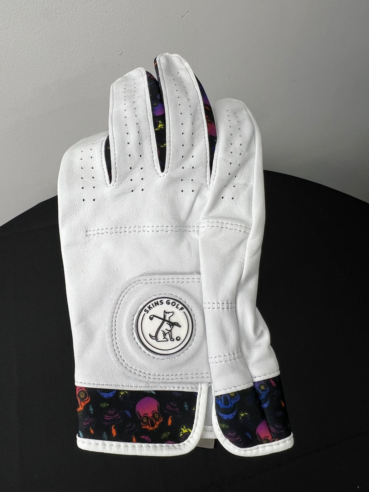 White golf glove with colorful skulls motif on cuff and between fingers, Skins Golf logo