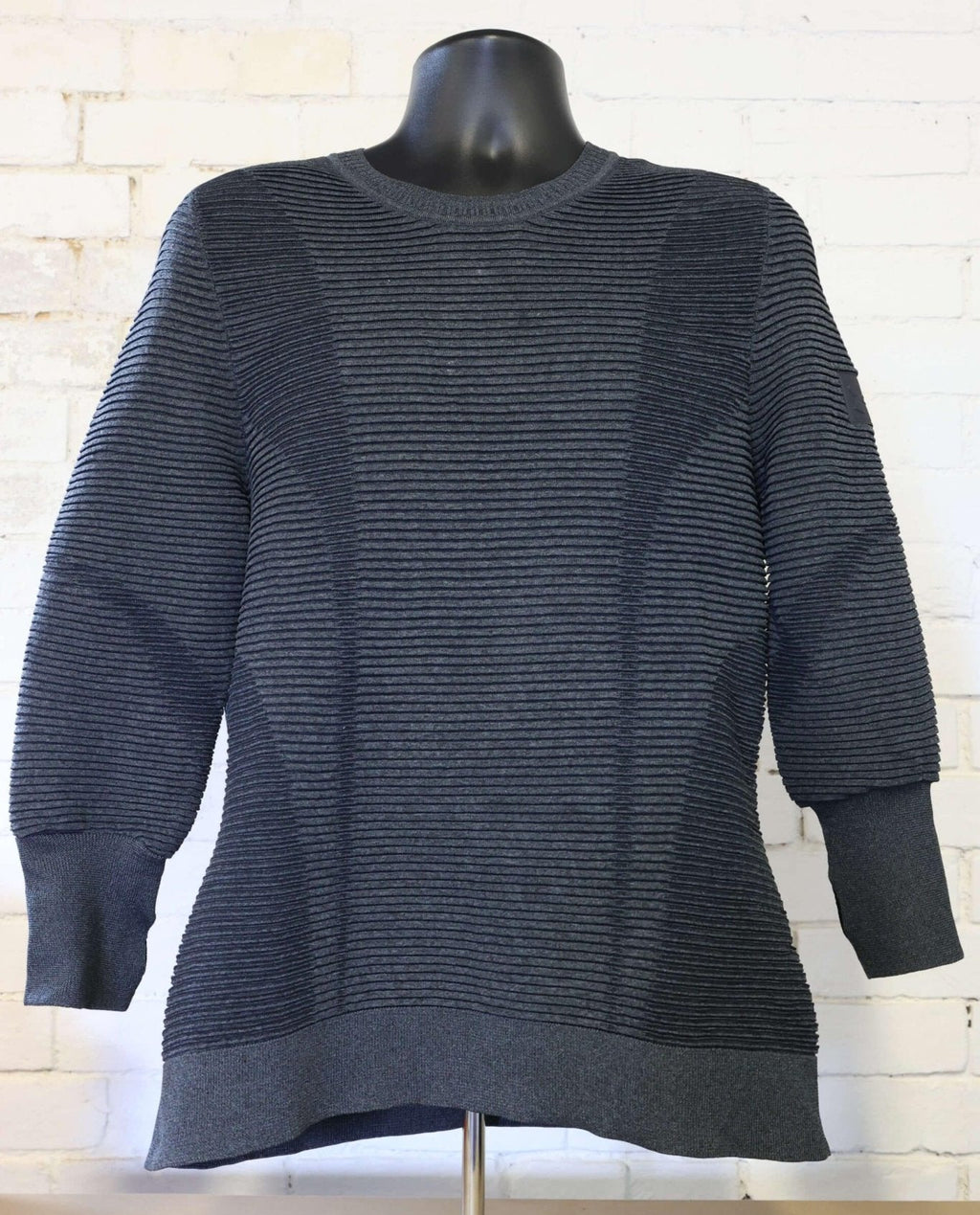 Front view of dark grey Under Armour jumper displayed on mannequin against white brick wall