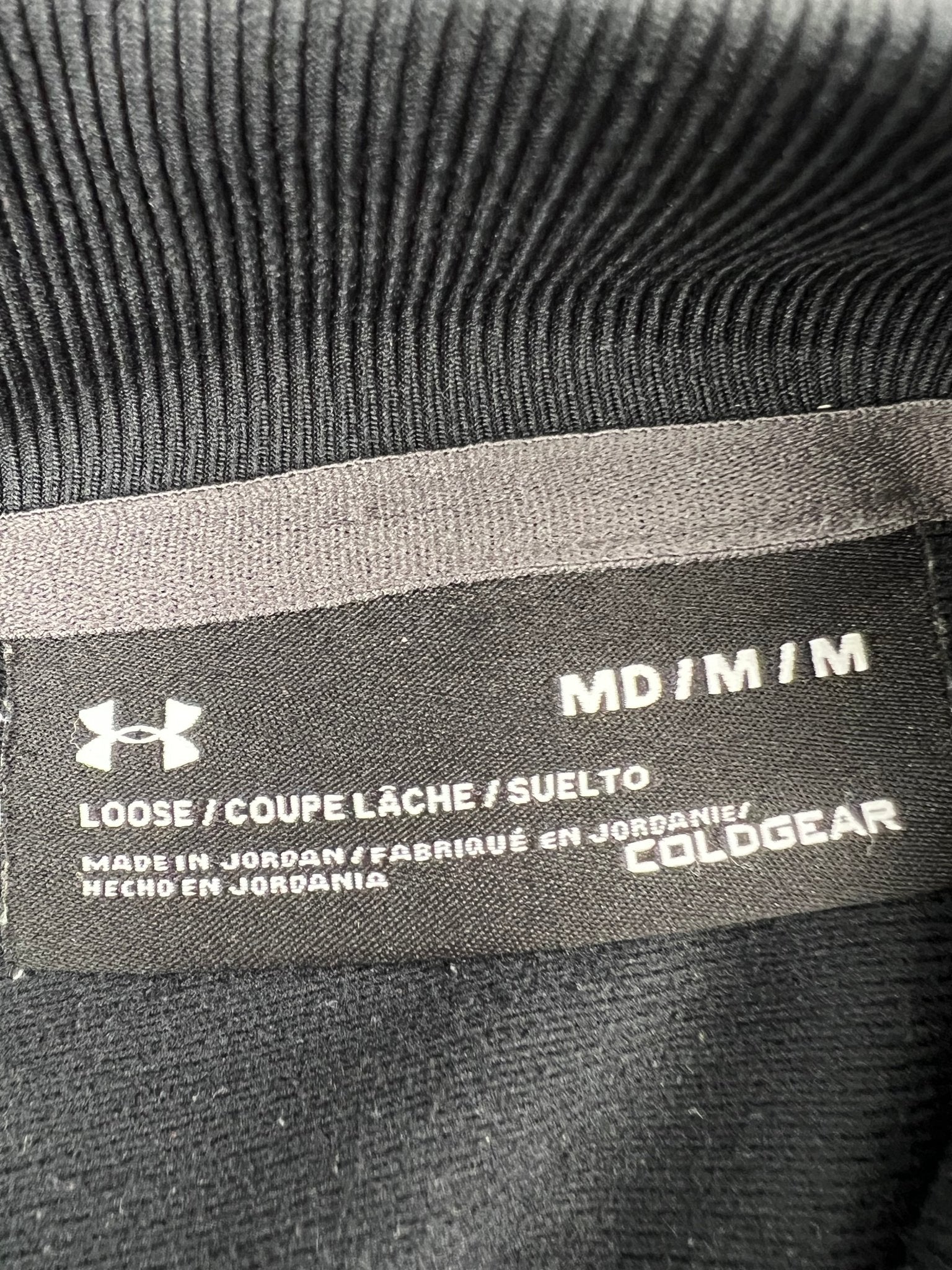 Brand and size label of Under Armour loose fitting black jacket showing ColdGear and medium size