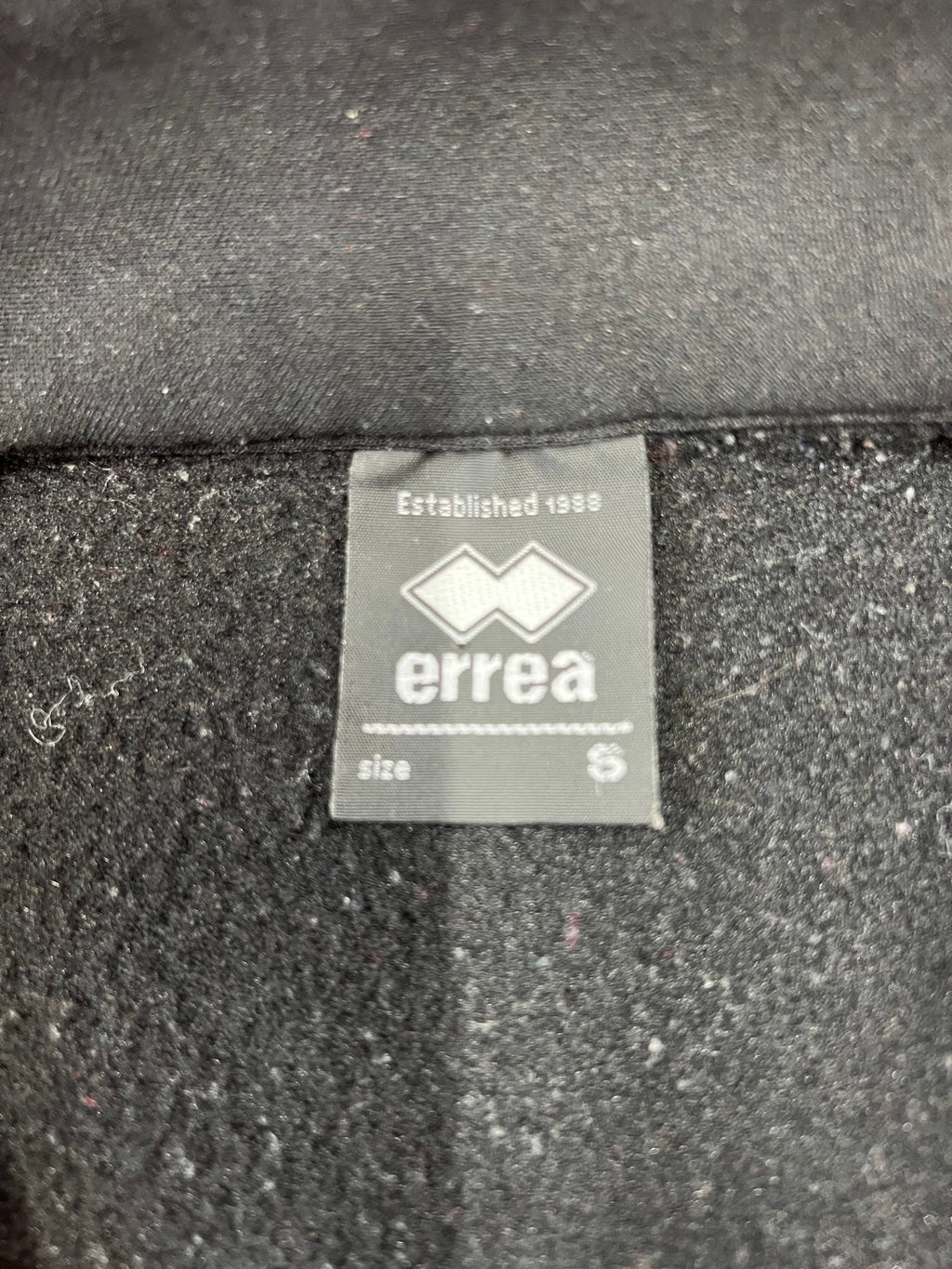 Close-up of Errea brand label and fleece inner lining inside the black volleyball top