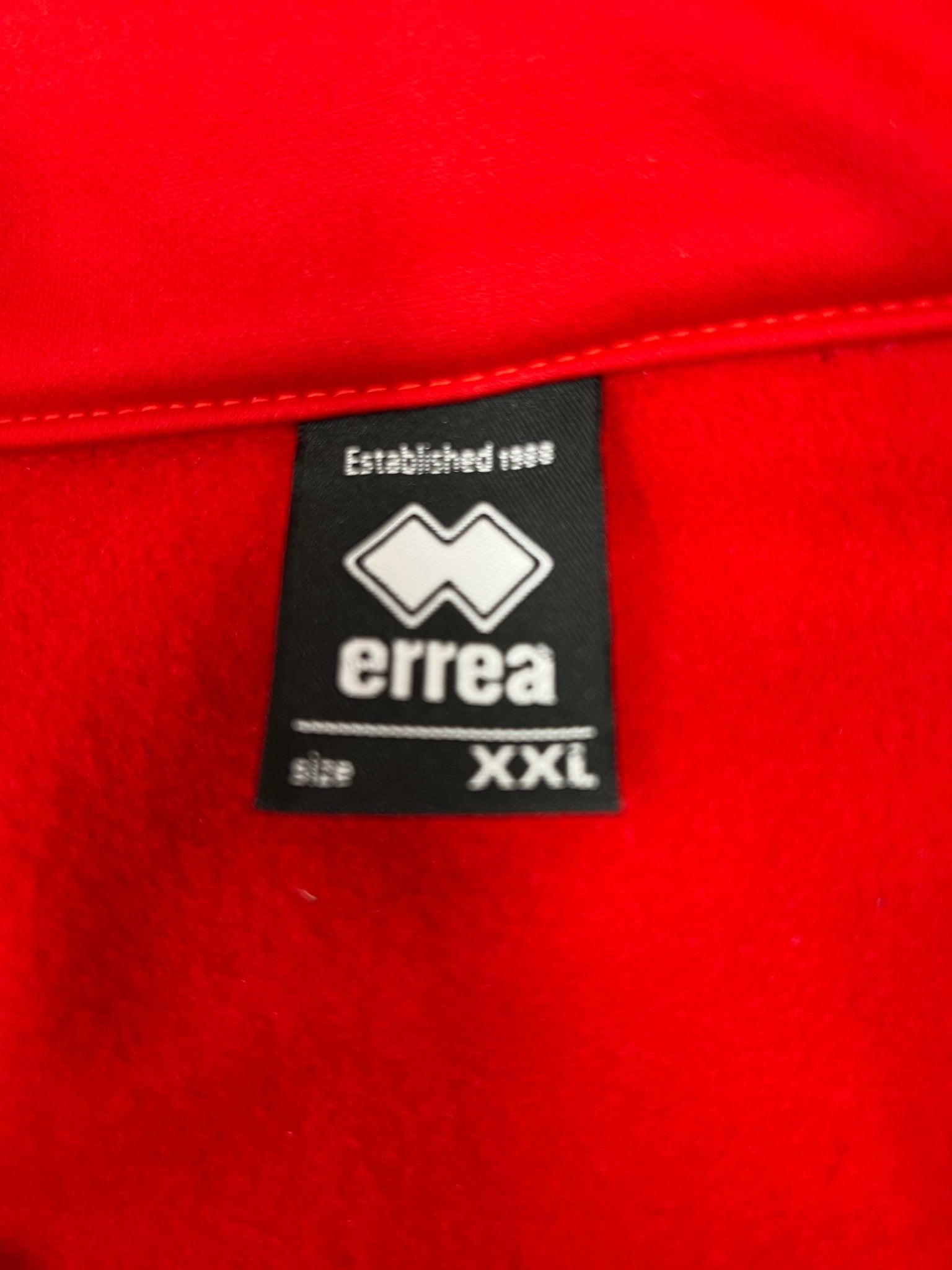 Close-up of internal tag showing Errea brand and XXL size on red jacket