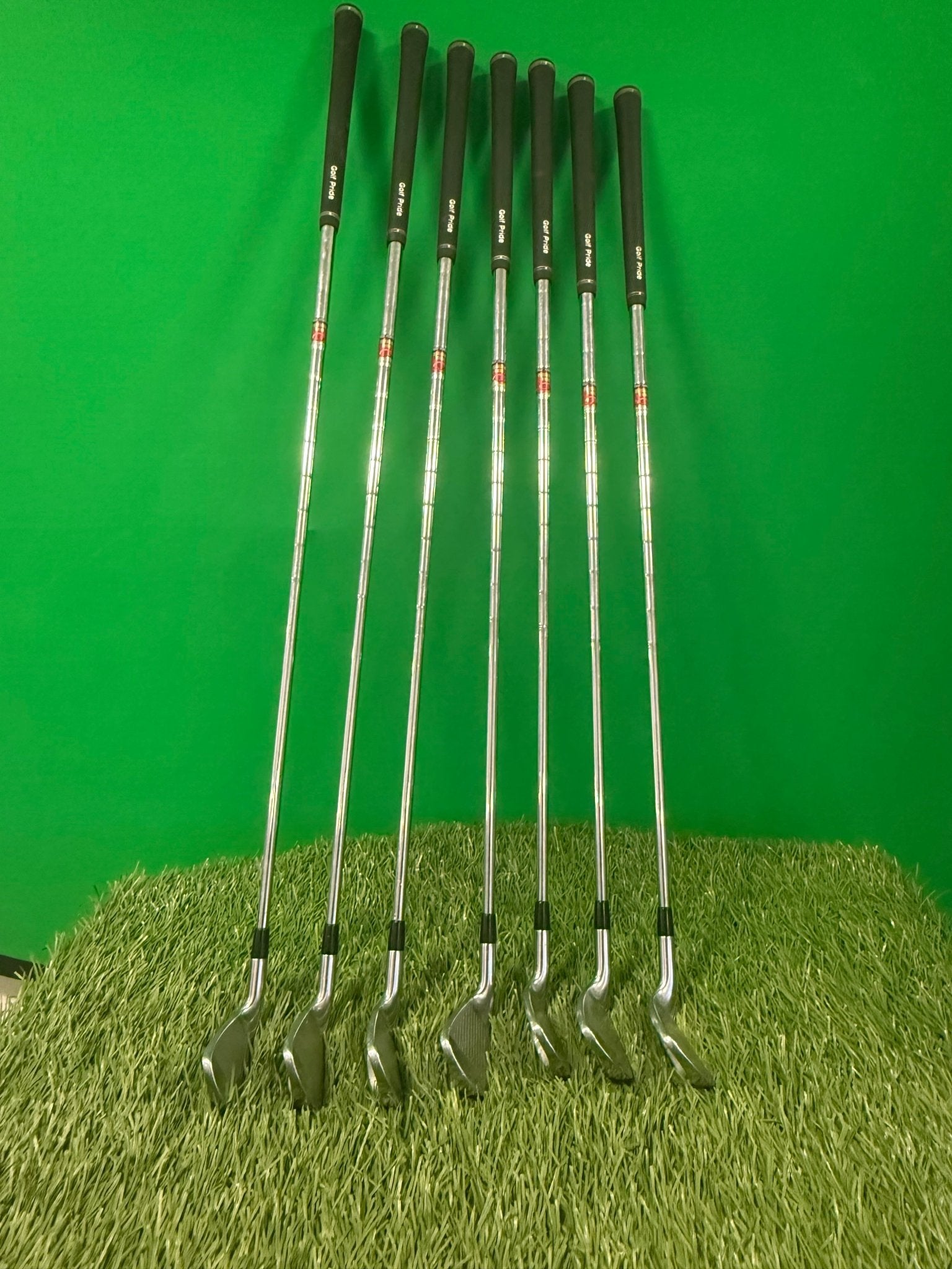 Set of seven Mizuno MX25 golf irons (4-PW) arranged on artificial turf with green background
