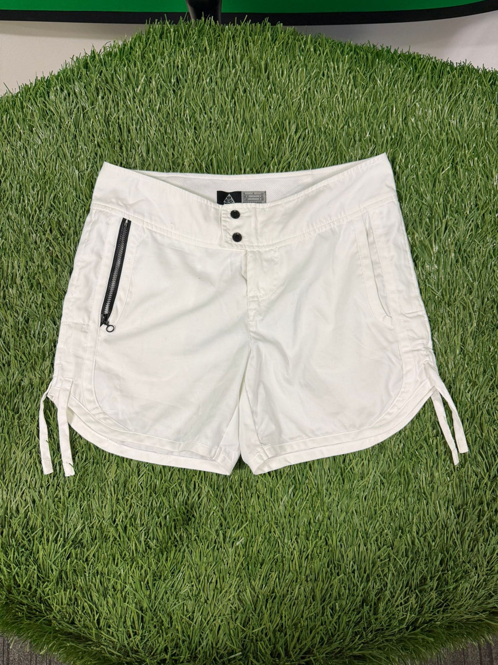 Front view of Nike ACG women's white tennis shorts with side zip pocket and adjustable hems.