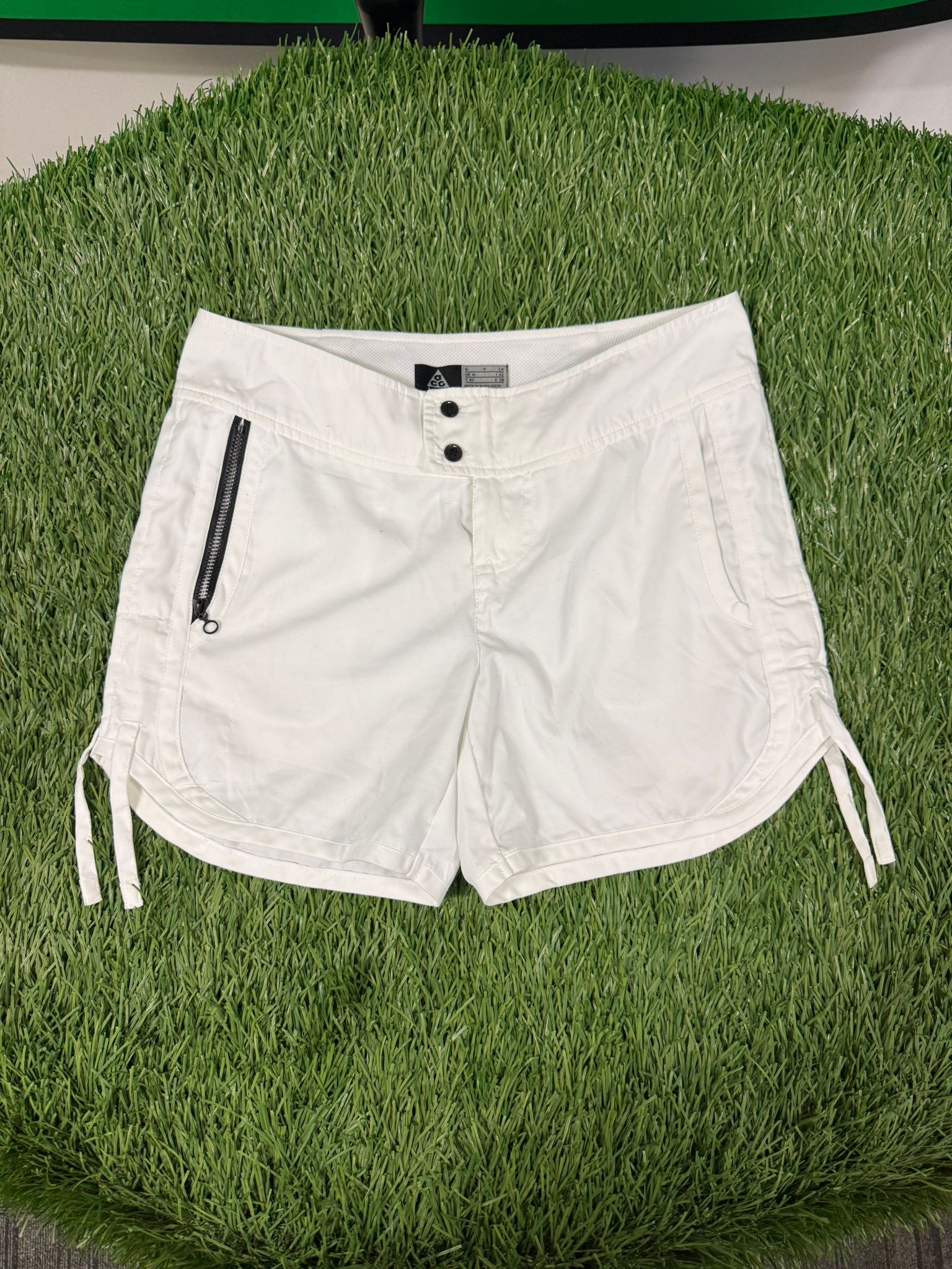 Front view of Nike ACG women's white tennis shorts with side zip pocket and adjustable hems.
