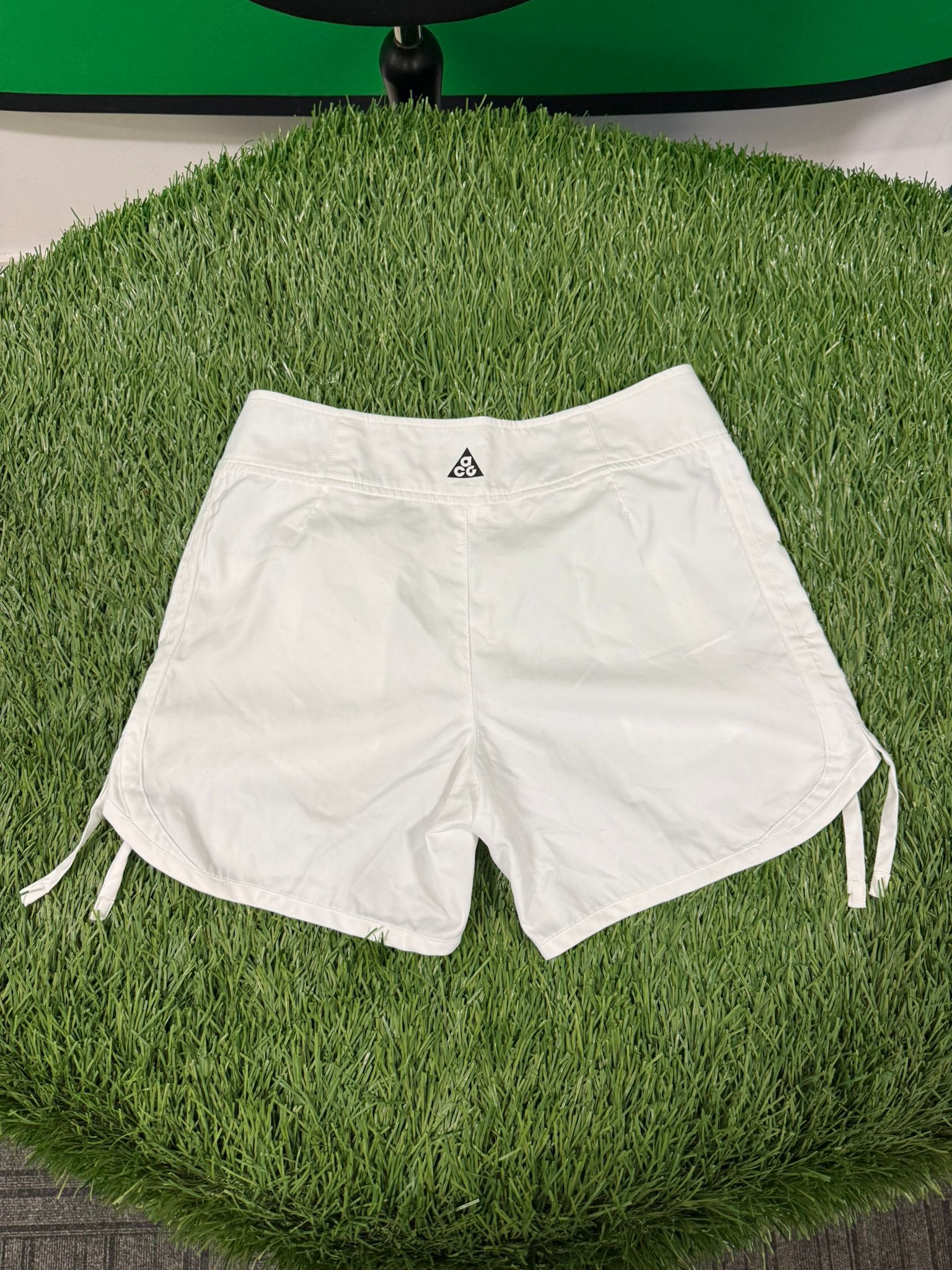 Back view of Nike ACG women's white tennis shorts showing ACG logo and drawstring details.