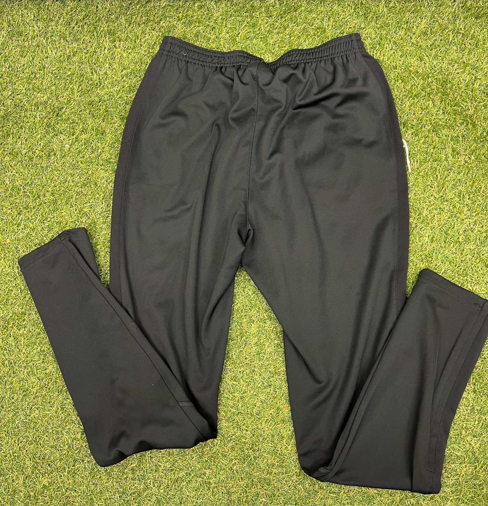 Back view of black Nike tracksuit trousers laid flat on grass