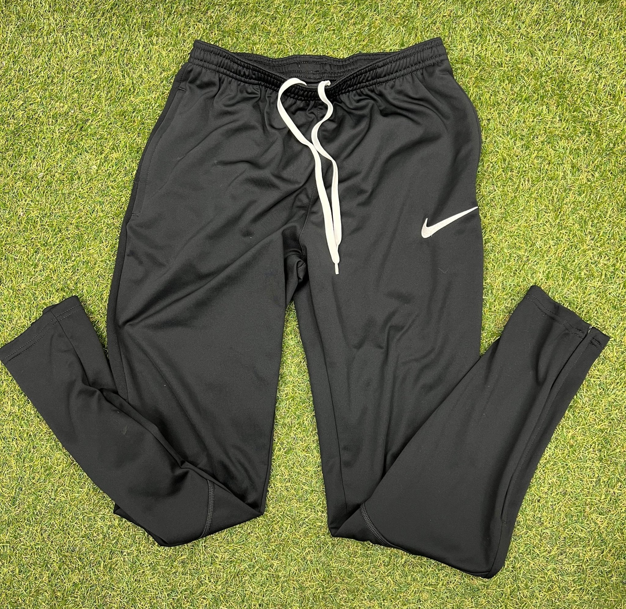 Front view of black Nike tracksuit trousers with white drawstring on grass background