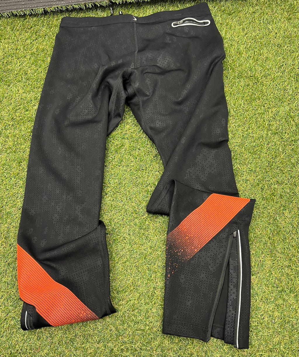 Back view of the same Nike running tights showing back pocket and ankle zips on grass