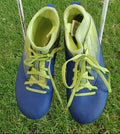 Top view of Kipsta kids football boots in blue and yellow on grass