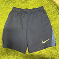 Navy blue Nike football shorts with yellow swoosh logo on green grass