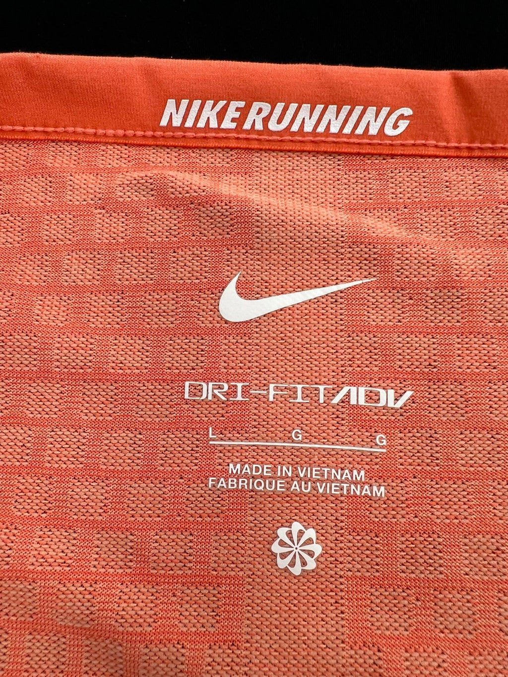 Close-up of Nike Running logo and Dri-FIT ADV label inside orange t-shirt
