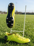 Nike Mercurial yellow football boots with black sole and conical studs displayed on a football pitch