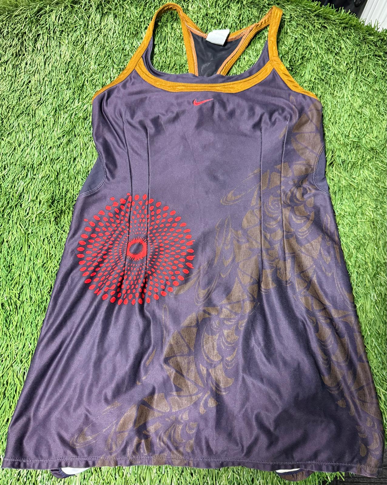 Purple Nike tennis dress with red and gold graphic print, racerback straps, laid on grass background