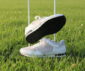 Pair of white and black trainers on display stand with green background