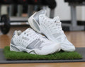 Pair of white and grey Prince trainers with mesh panels and rubber soles displayed on a stand