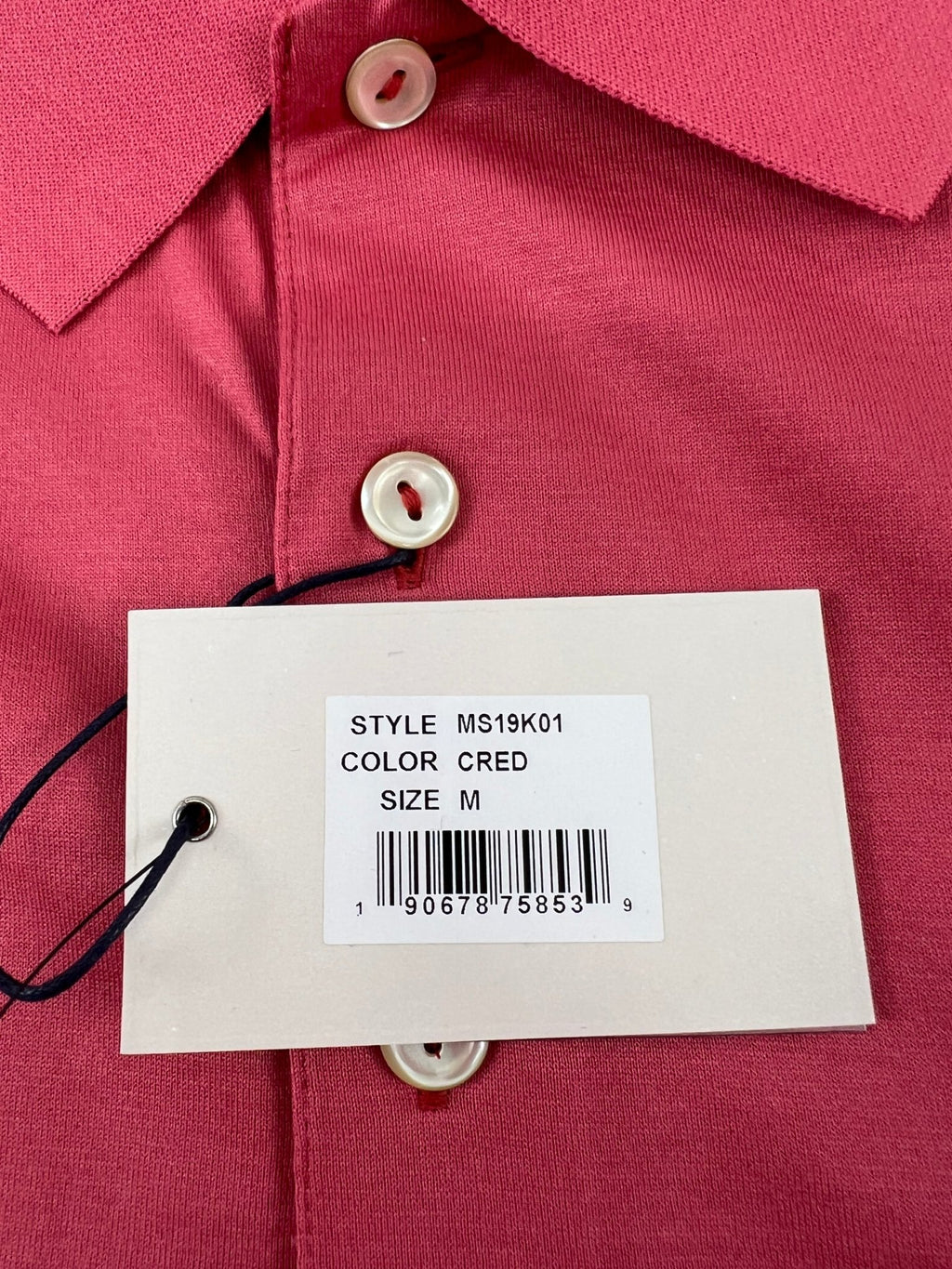 Close-up of tag showing style MS19K01, color CRED, size M on pink Peter Millar polo