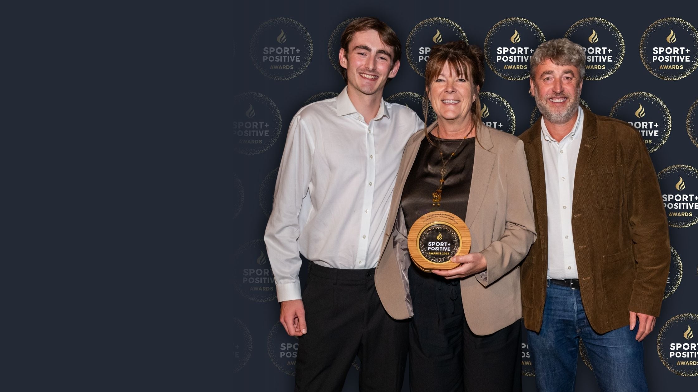 Three people holding an award in front of a branded backdrop
