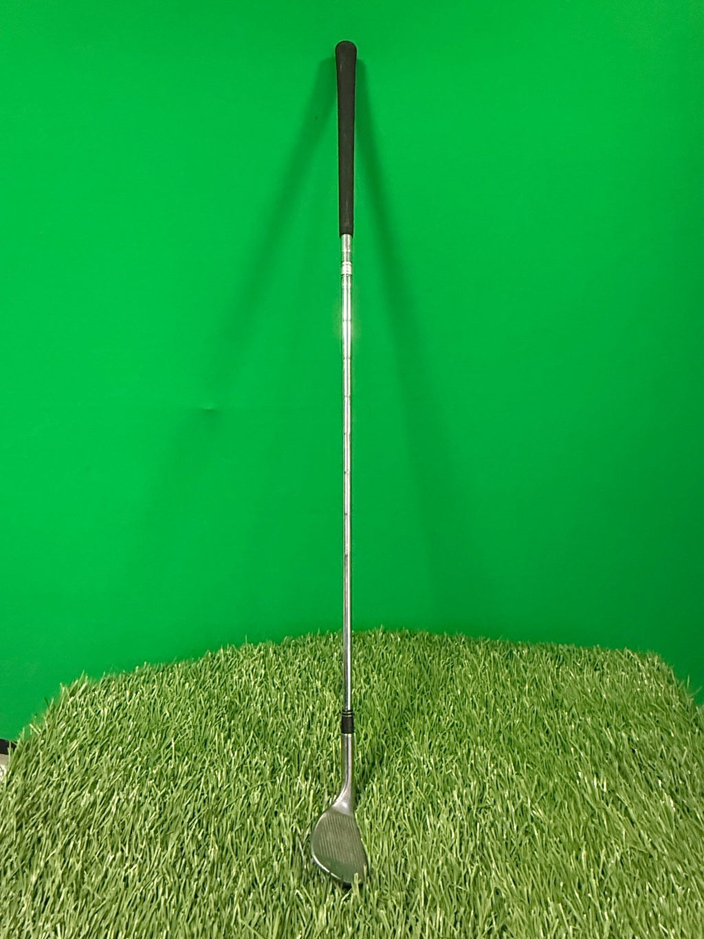 Taylormade 60 degree golf wedge standing on artificial grass with green background