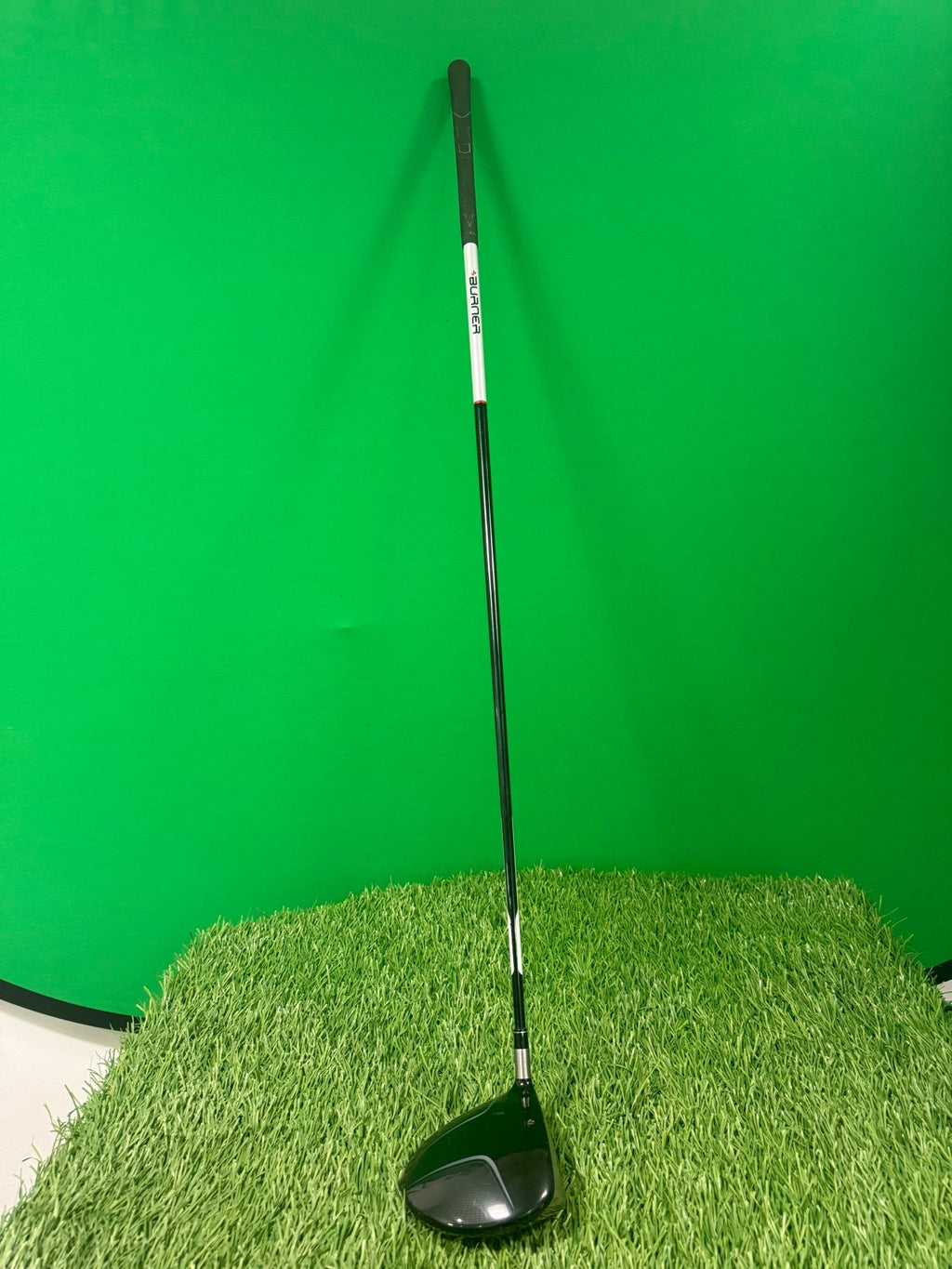 TaylorMade Burner Draw Driver standing upright on artificial grass with green backdrop