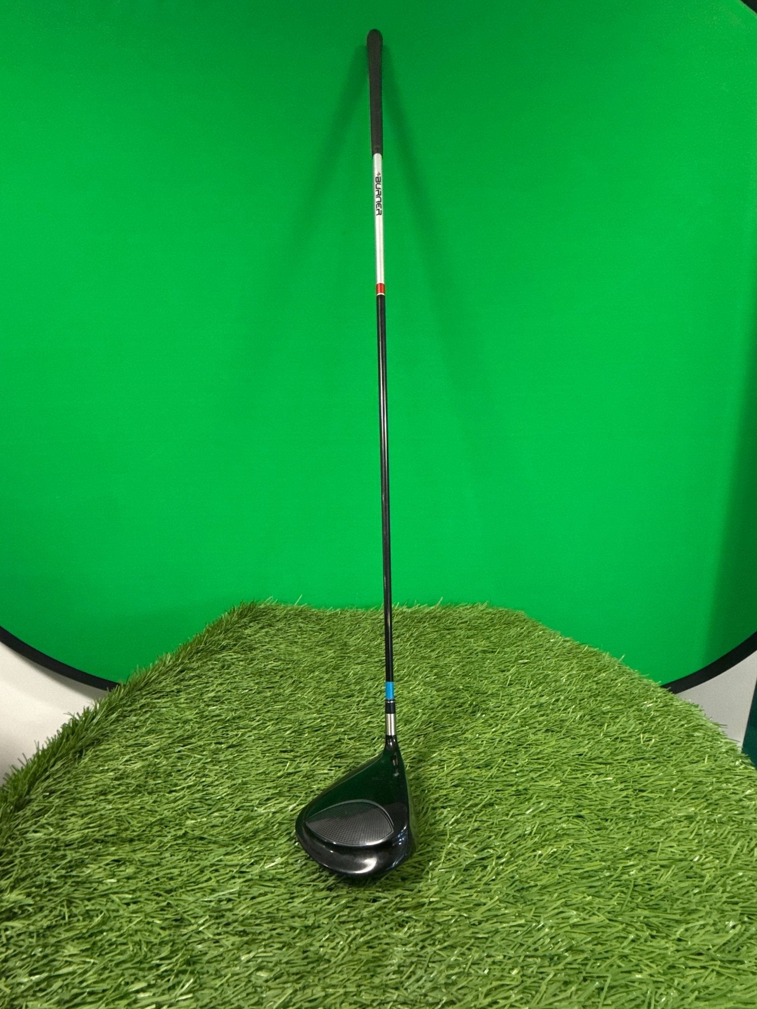 Used TaylorMade Burner driver golf club standing on artificial grass with a green background