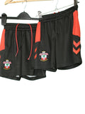 Two pairs of black and red Southampton FC kids football shorts with club crest shown on hangers