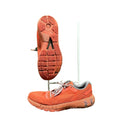 Side and sole view of orange Under Armour Machina 2 running trainers on artificial grass