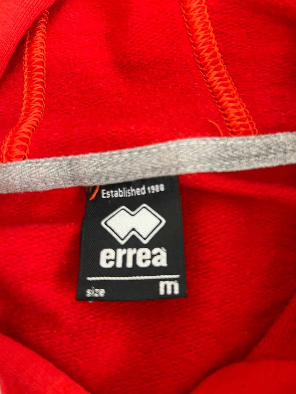 Close-up of the Errea brand label inside the Volleyball England red hoodie showing medium size