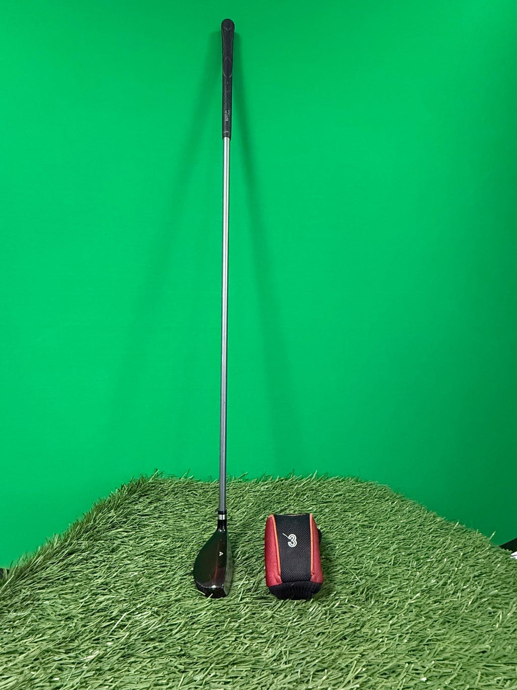 Wilson Deep Red 3 Hybrid golf club with headcover on artificial grass and green background