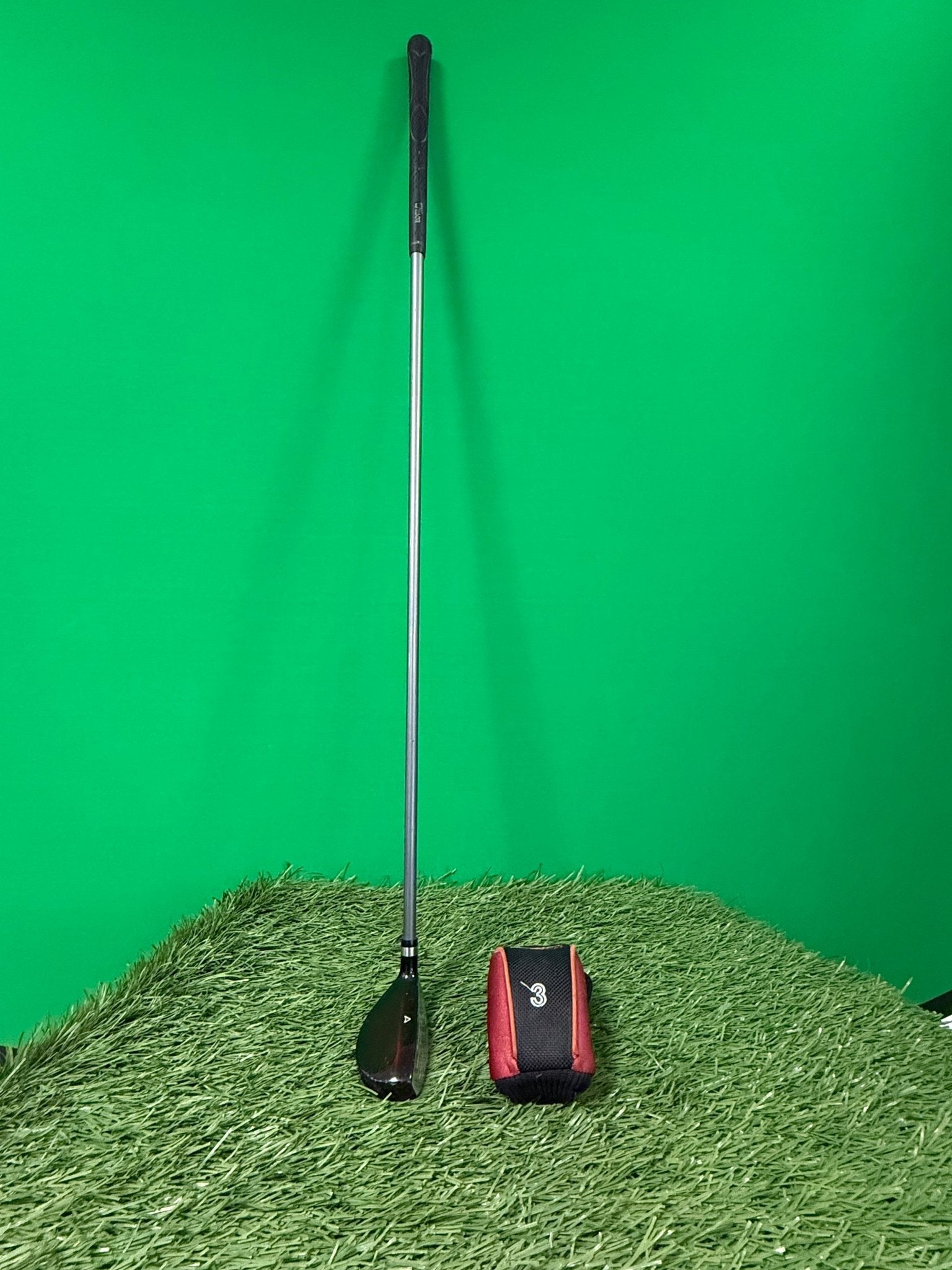Wilson Deep Red 3 Hybrid golf club with headcover on artificial grass and green background