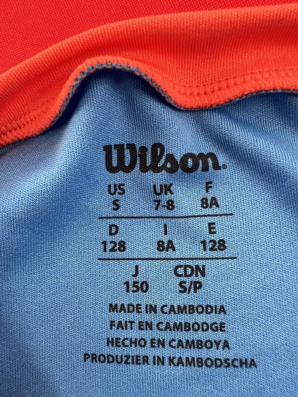Wilson light blue t-shirt for kids age 7-8 with orange collar accents. Lightweight, breathable fabric for tennis.