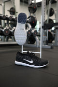 Black Nike Zoom training shoes with a white sole displayed on artificial grass, side and sole views visible