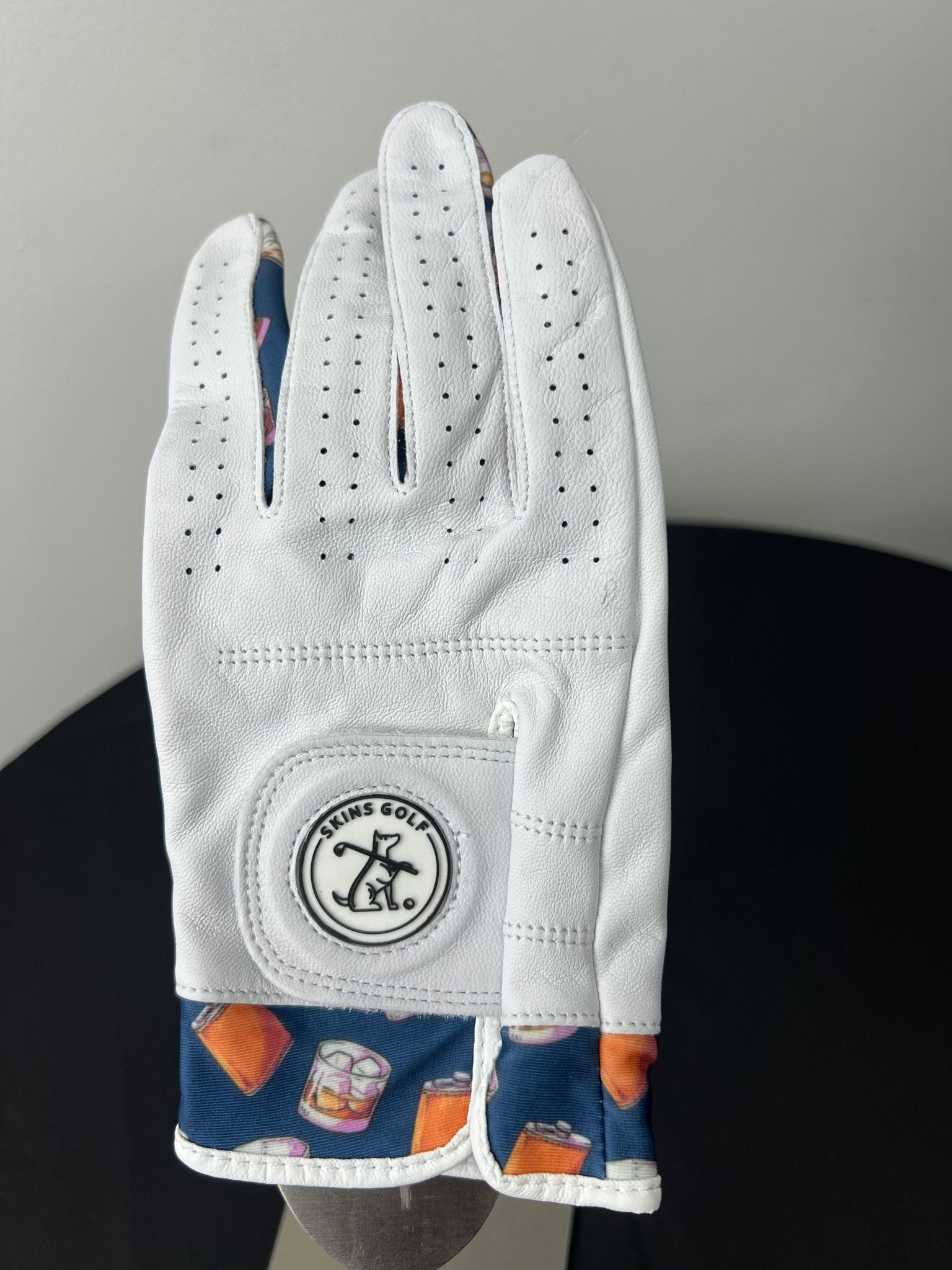 Women's white golf glove with whiskey motif cuffs and Skins Golf logo.
