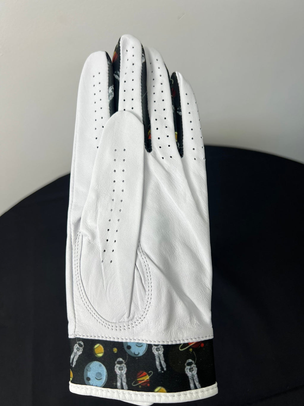 Rear view of women's white leather golf glove showing space motif detail at wrist and finger seams