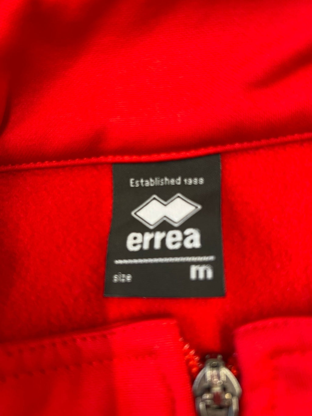Close-up of Errea brand label stitched inside the collar showing size M
