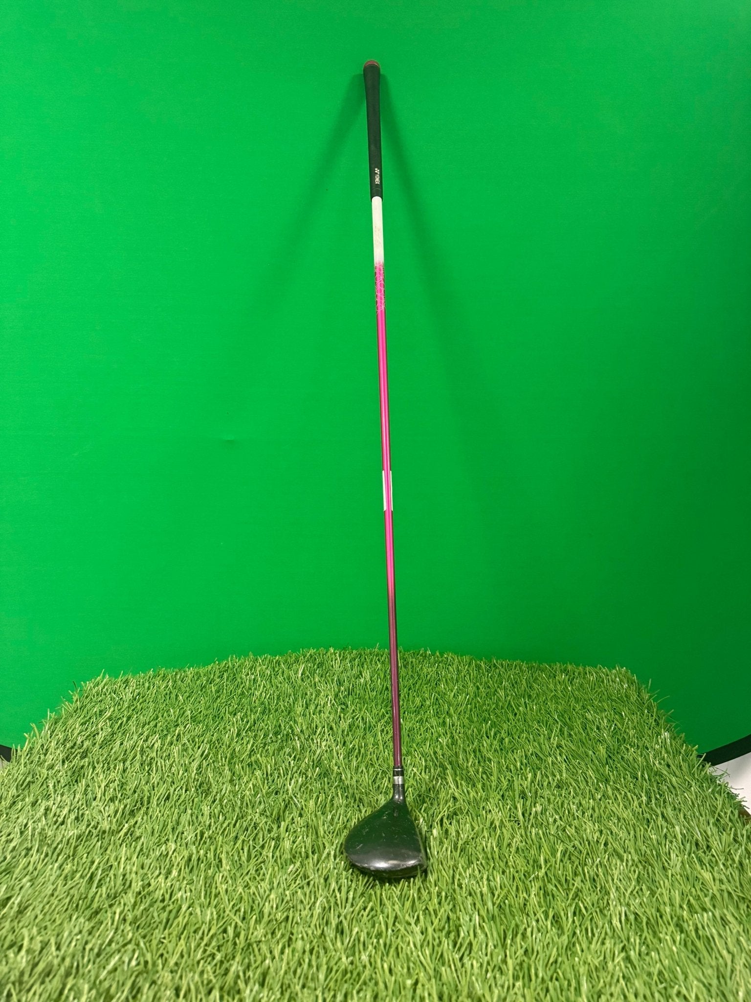 Yonex Ladies 5 wood golf club with pink and white shaft standing upright on artificial grass