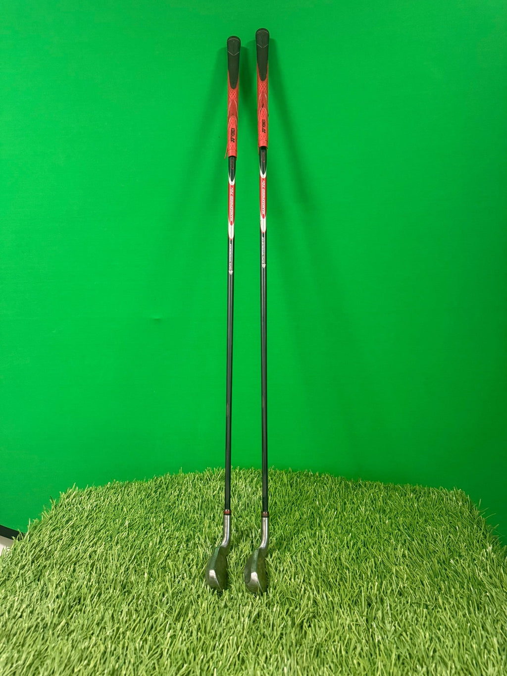 Pair of Yonex Nanospeed 4 & 5 hybrid golf clubs with red and black grips, standing upright on artificial grass against a green background