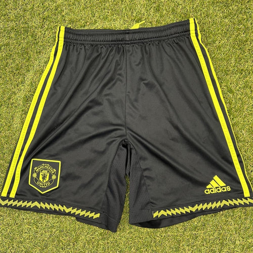 Front of Adidas Manchester United youth black shorts with yellow stripes and logos